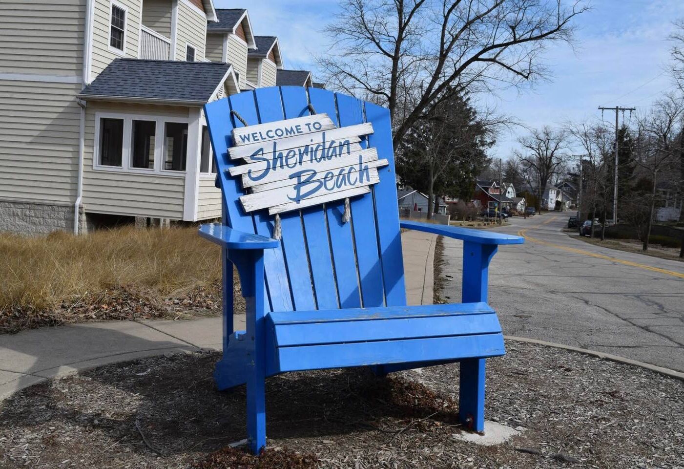 A blue Adirondack chair with a 'Welcome to Sheridan Beach' sign.