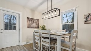 Une salle à manger avec une table et des chaises en bois, un luminaire suspendu et un tableau au mur.