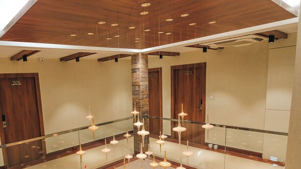 A multi-level interior with a central staircase, wooden ceiling, and hanging pendant lights. - New Hotel Snow Crest (Joshimath)