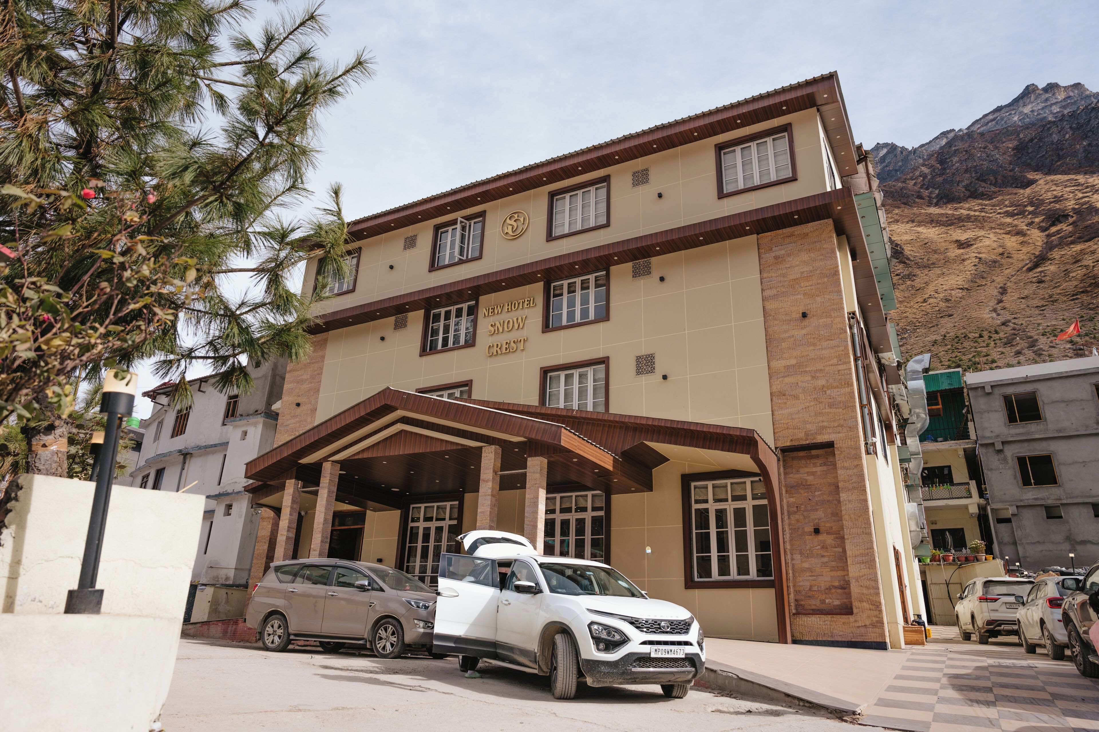 A hotel named "New Hotel Snow Crest" with a modern architectural design, featuring a prominent entrance and a view of the surrounding mountainous landscape.