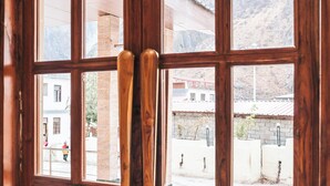 A wooden door with a handle, large windows, and a view of buildings and a mountain in the background. - New Hotel Snow Crest (Joshimath)
