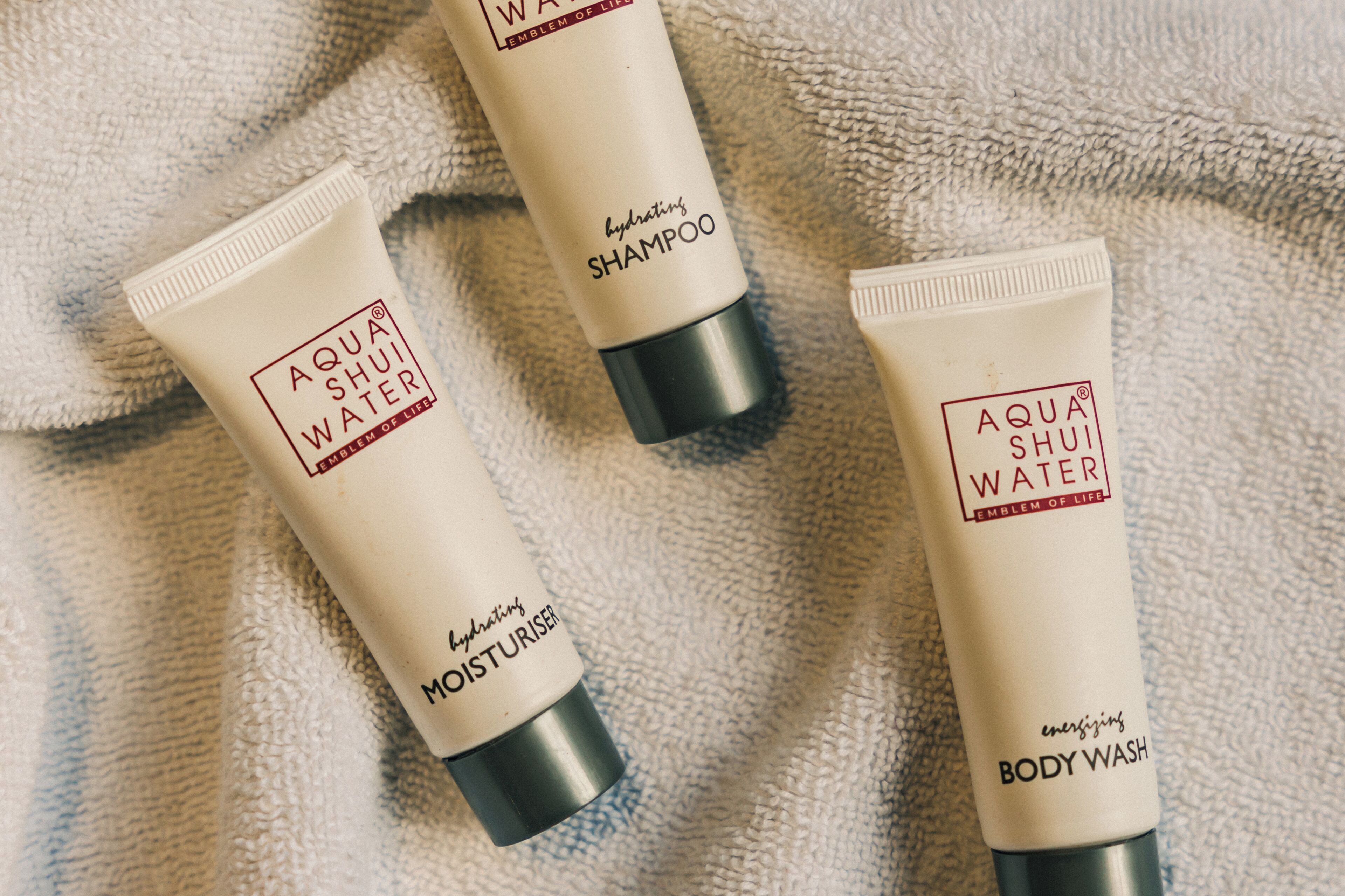 Three tubes of AQUA SHUI WATER product on a textured fabric surface.