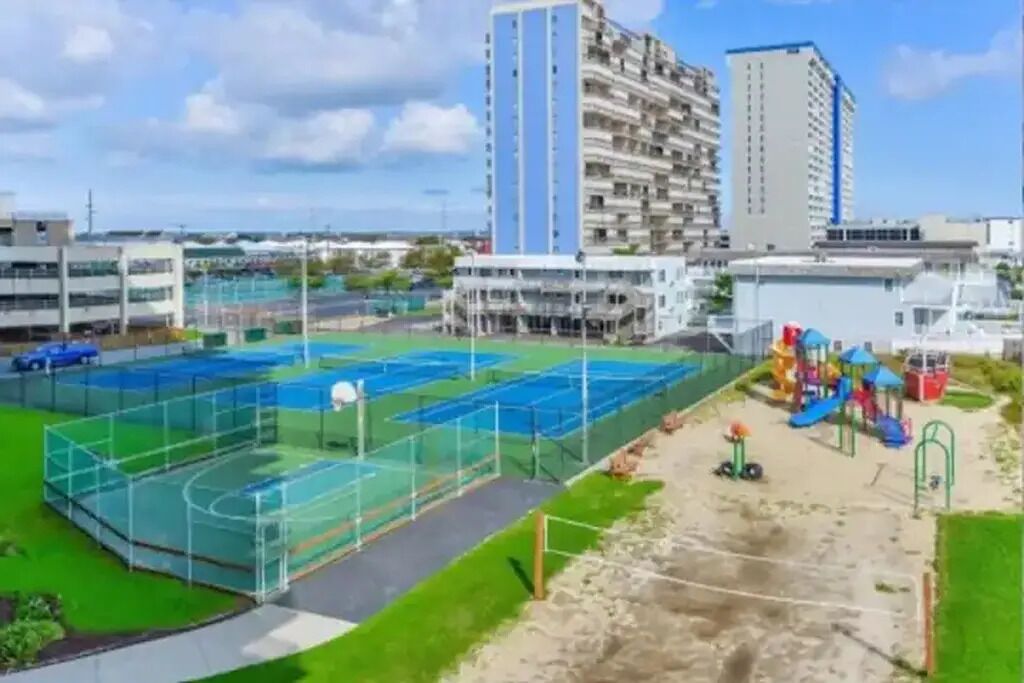Una cancha deportiva con un parque infantil y un edificio alto al fondo.