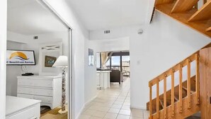Een hal met een witte trap, een bed, een dressoir en een lamp.