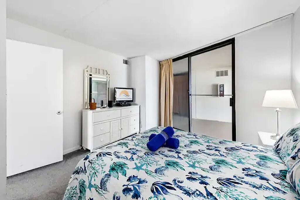 A hotel room with a bed, a dresser, a television, and a sliding door.