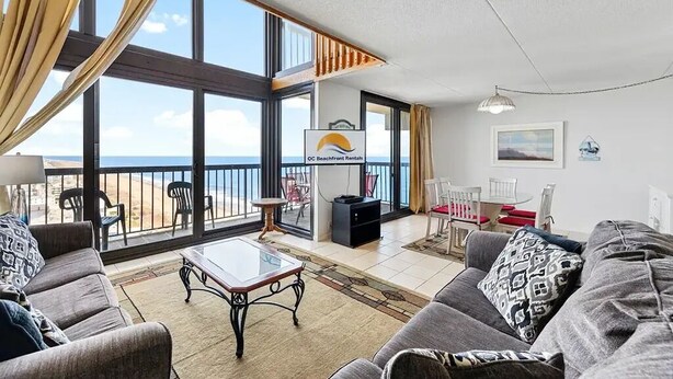 Ein geräumiges Wohnzimmer mit Balkon, großen Fenstern und Blick auf den Strand.