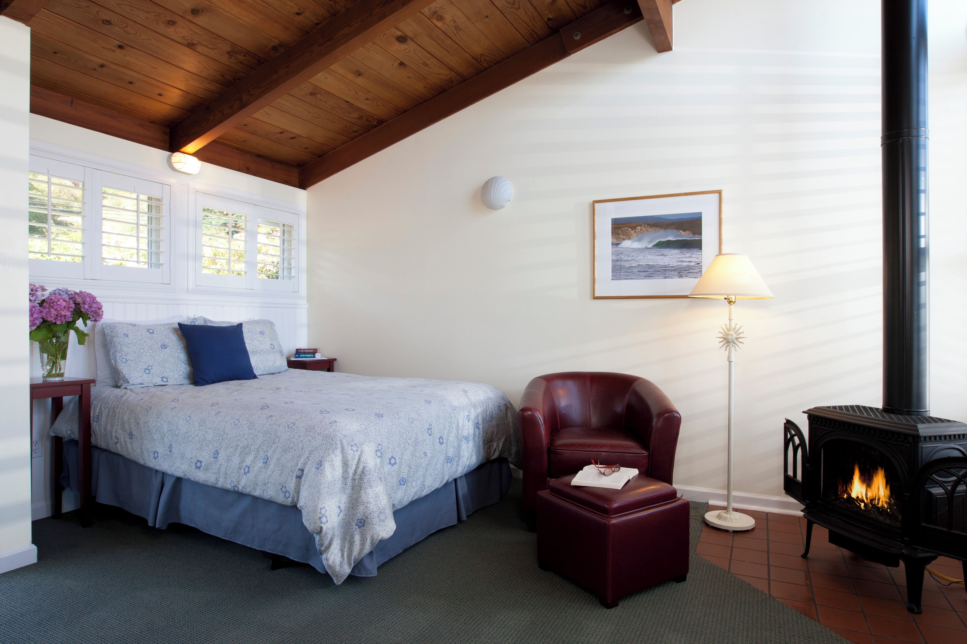A bedroom with a bed, a red armchair, a standing lamp, and a fireplace.