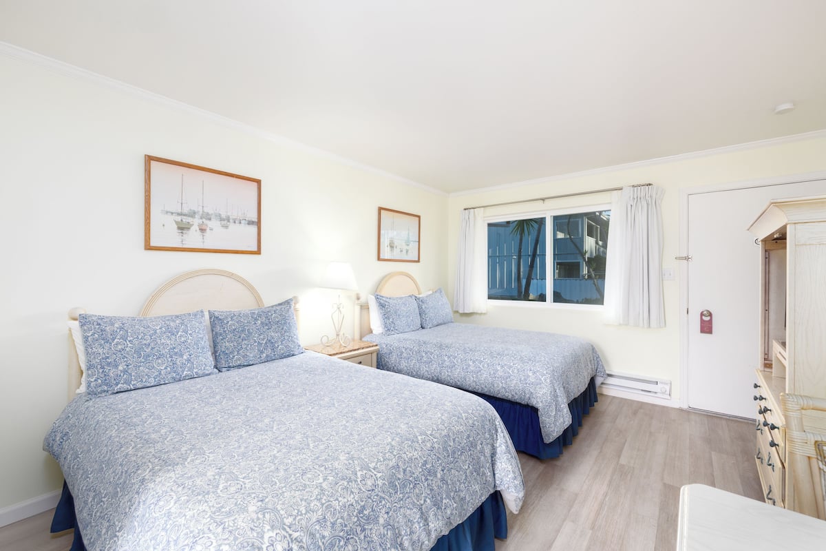 Une chambre avec deux lits, une fenêtre avec des rideaux, une porte et une petite table avec une lampe.