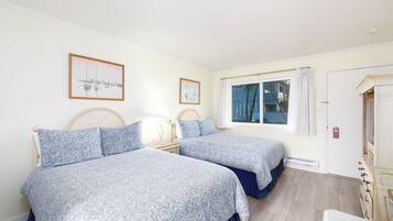 Una habitación con dos camas, una ventana con cortinas, una puerta y una mesita de noche con lámpara.