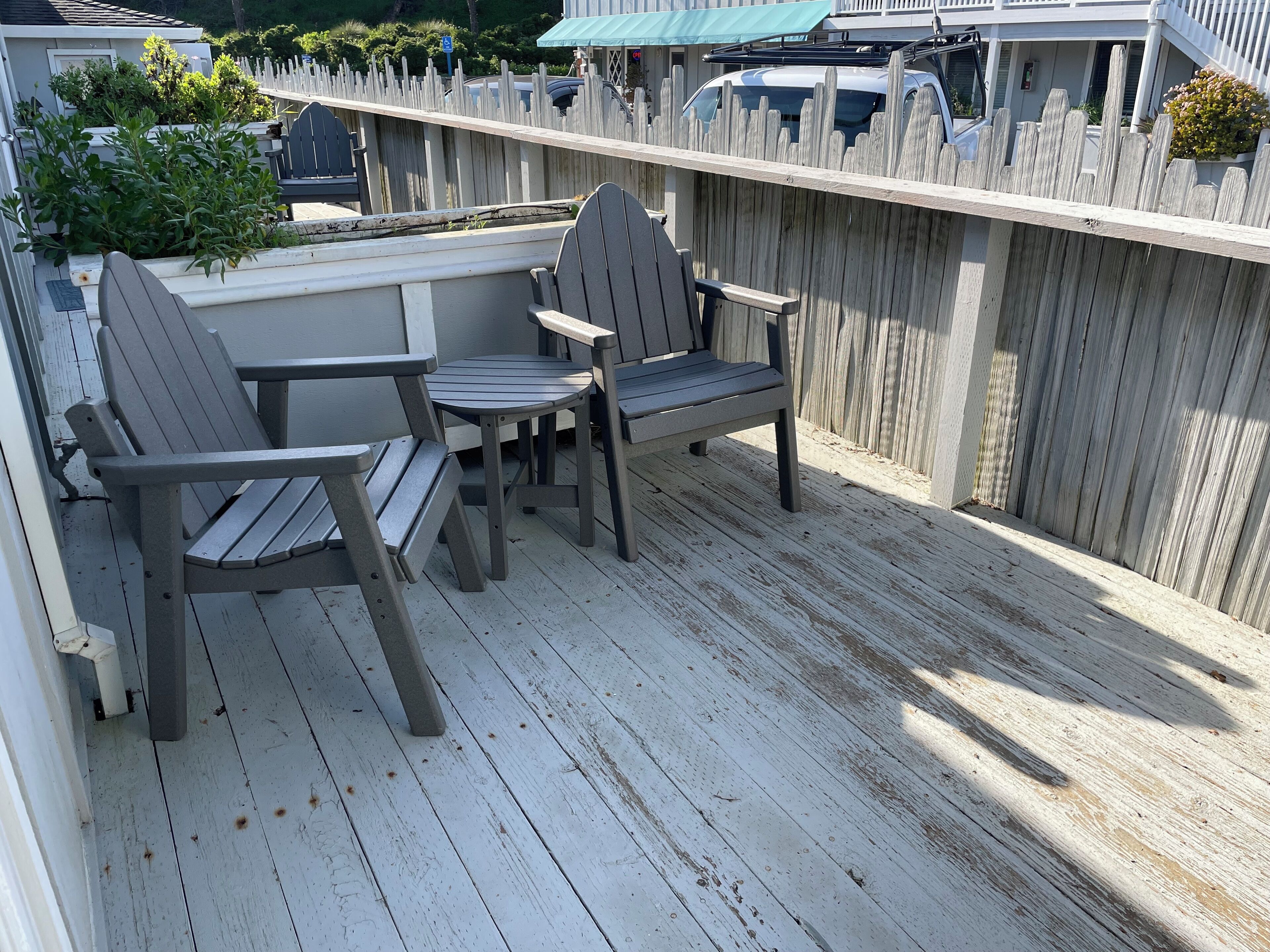 A deck with two Adirondack chairs and a small table, surrounded by a wooden fence.