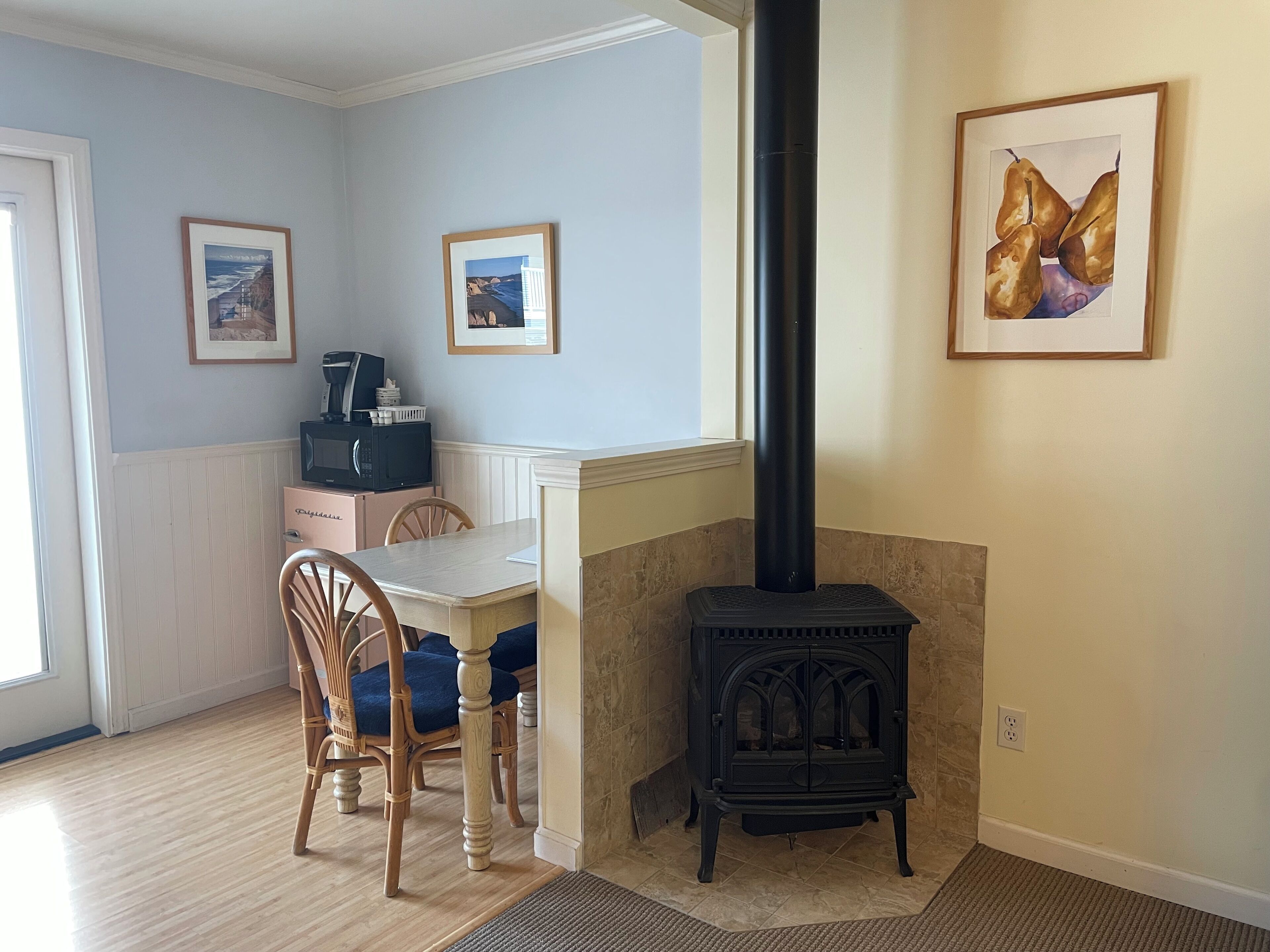 A dining area with a table and chairs, a black wood-burning stove, and framed artwork on the walls.