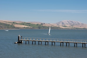 A pier extending into calm water with a sailboat in the distance and hills in the background. - Tomales Bay Resort and Marina (Inverness)