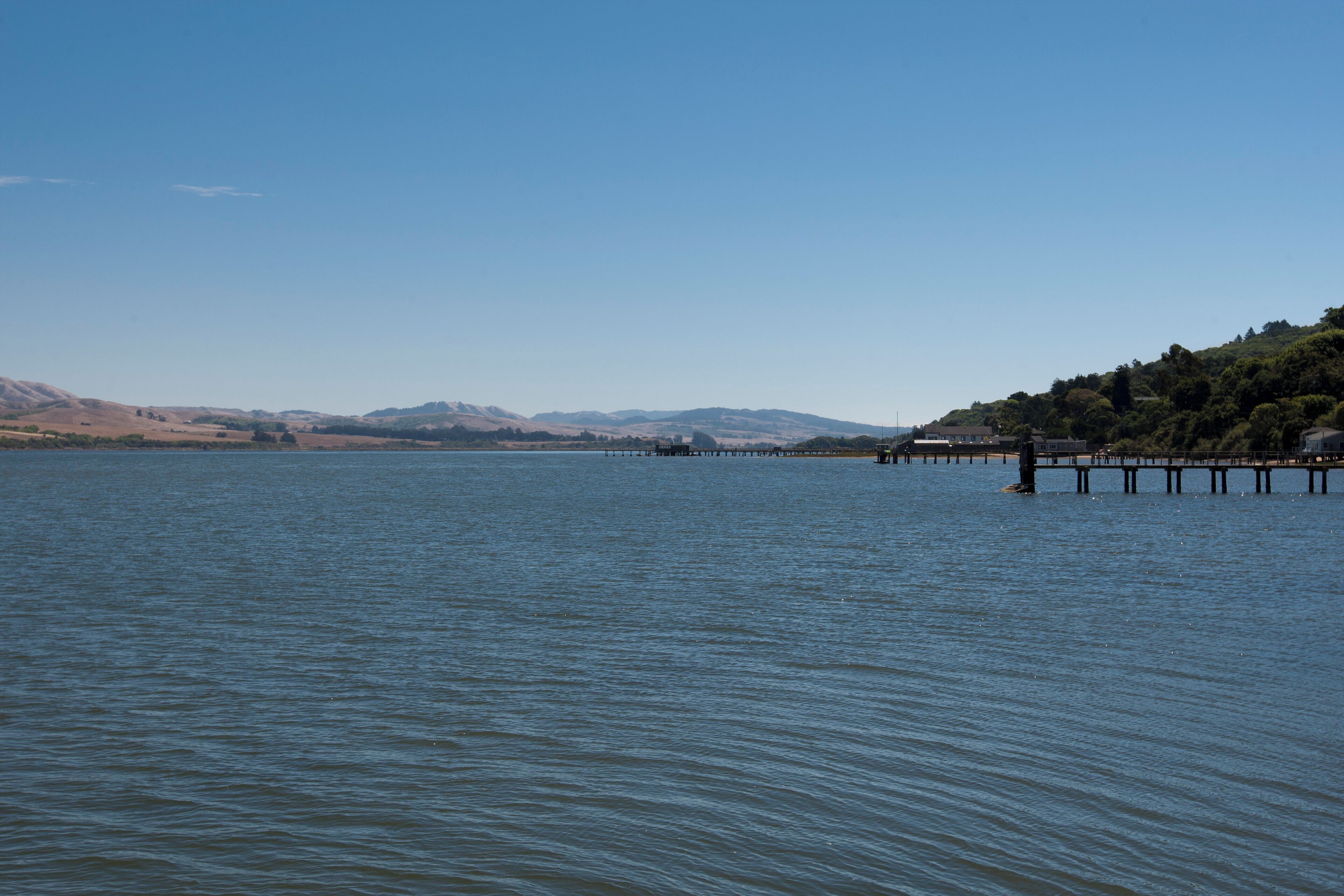 Un lago tranquilo con un muelle que se adentra en el agua, rodeado de colinas y cielos despejados.