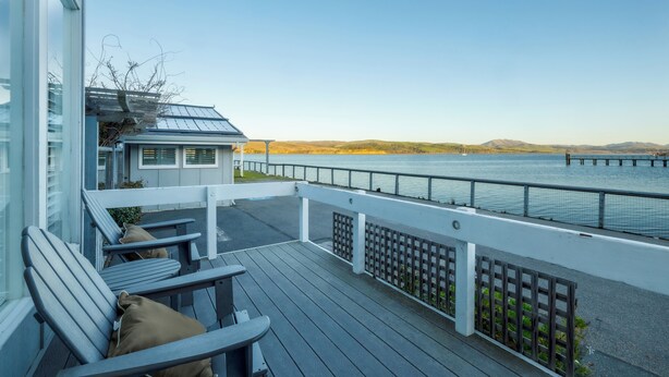 Een houten terras met stoelen en uitzicht op water.