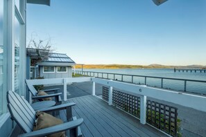 Eine Holzterrasse mit Stühlen und Blick auf ein Gewässer.