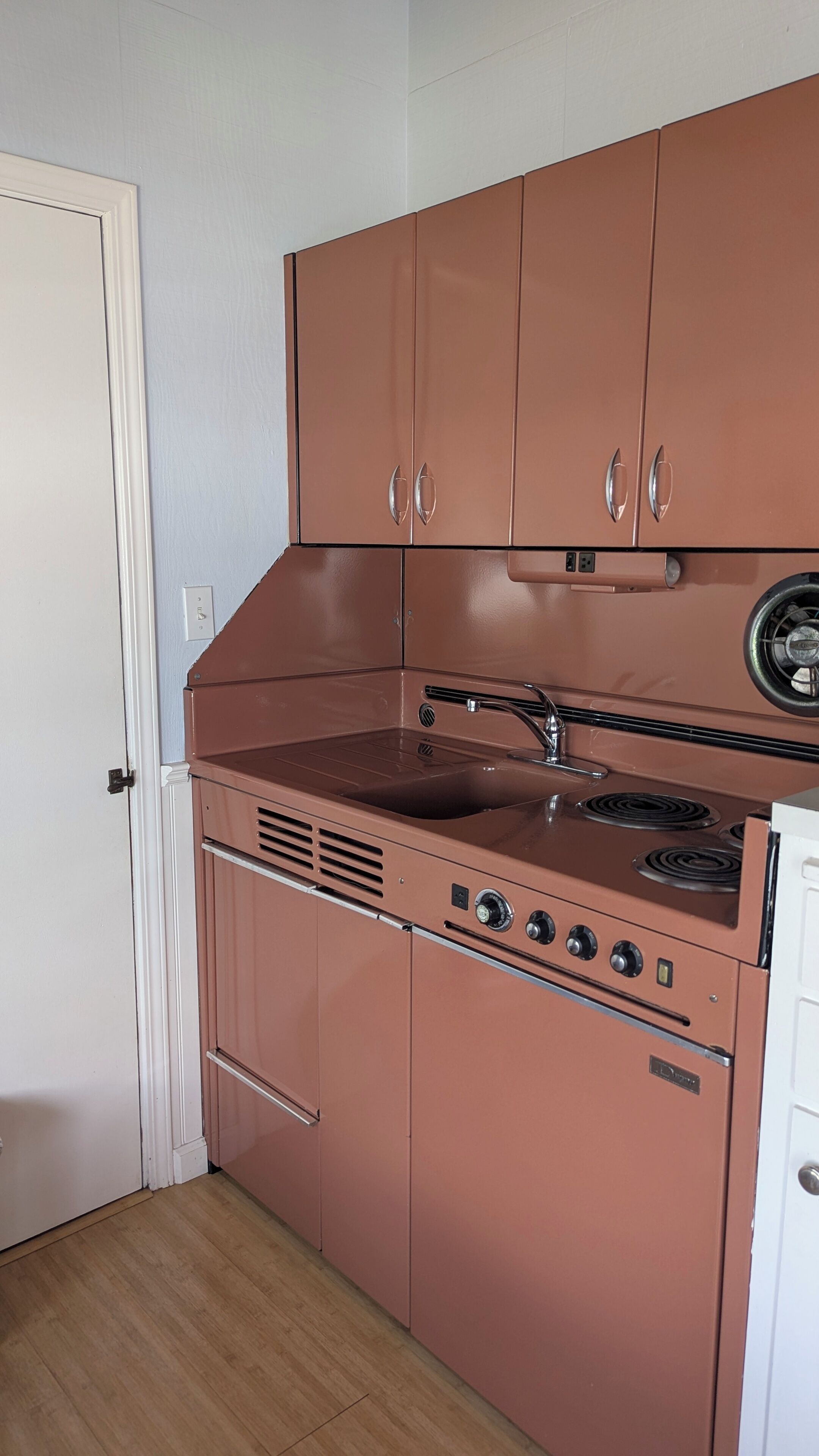 Una cocina compacta con estufa integrada, lavamanos y armarios superiores.