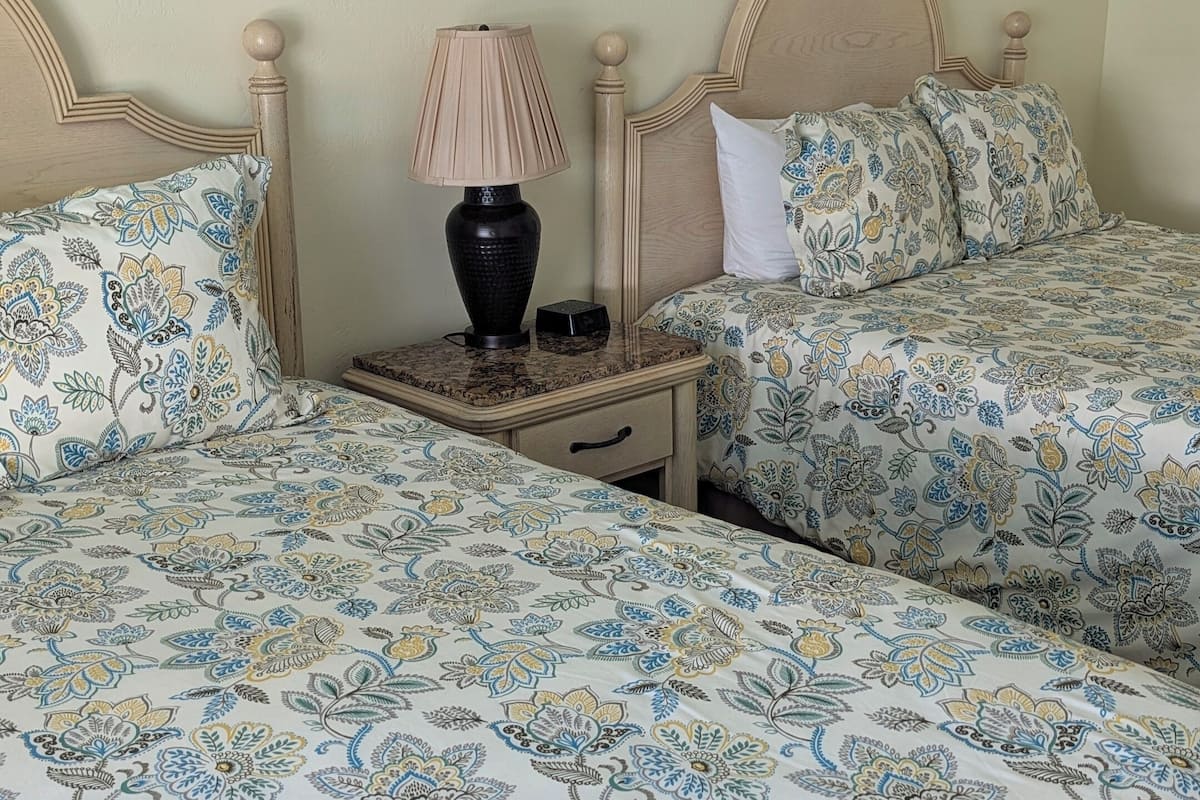 Une chambre avec deux lits, une table de chevet, une lampe et une petite table.