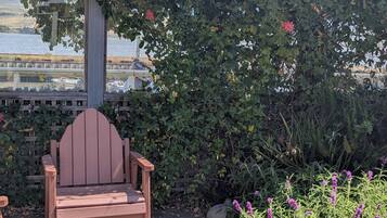 A wooden chair under a vine-covered structure with a view of the water and boats.
