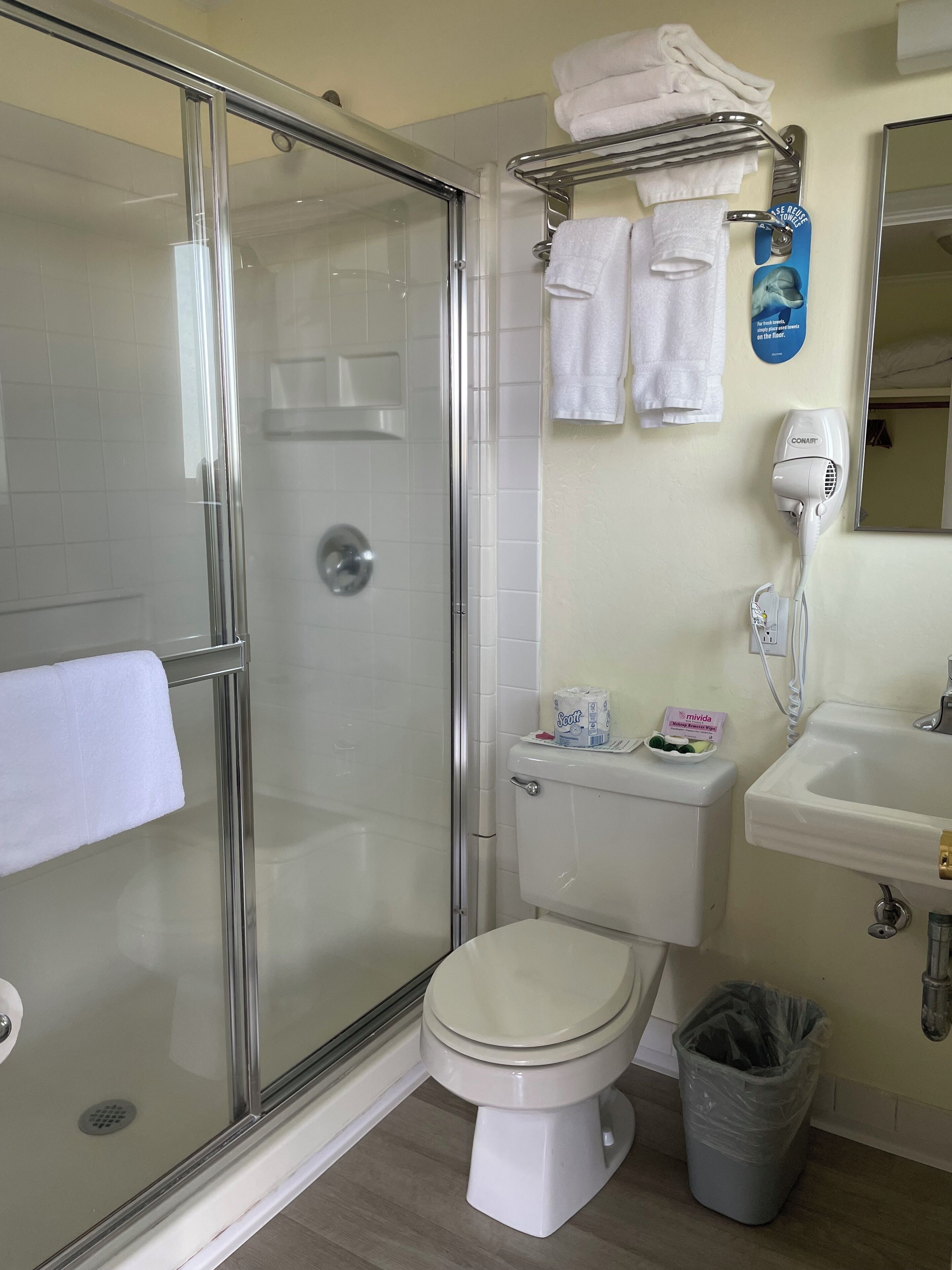 Baño con cabina de ducha de vidrio, inodoro, lavabo y cubo de basura.