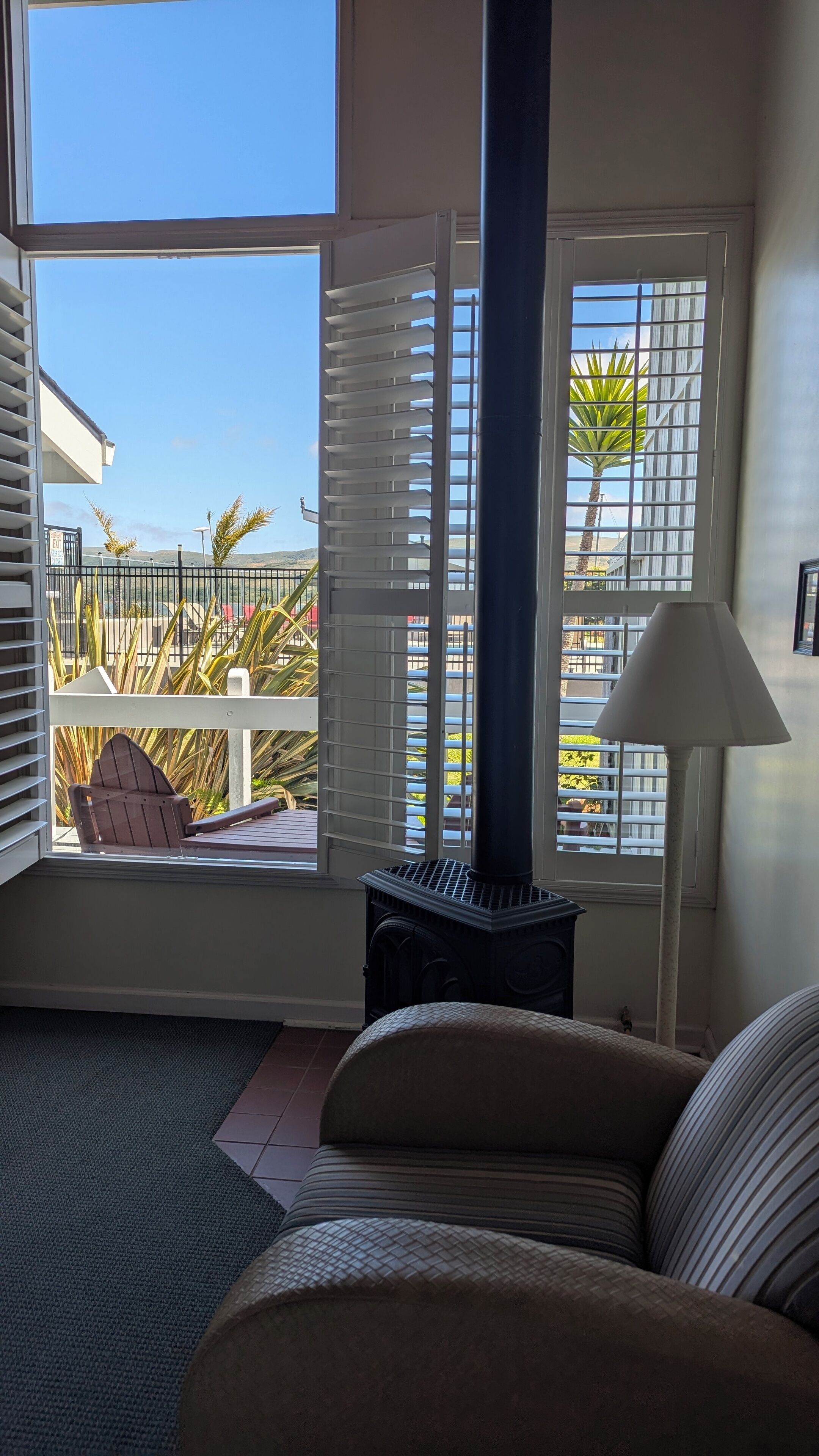 Ein Zimmer mit einem großen Fenster, einem Sofa, einer Lampe und einem kleinen Heizgerät.