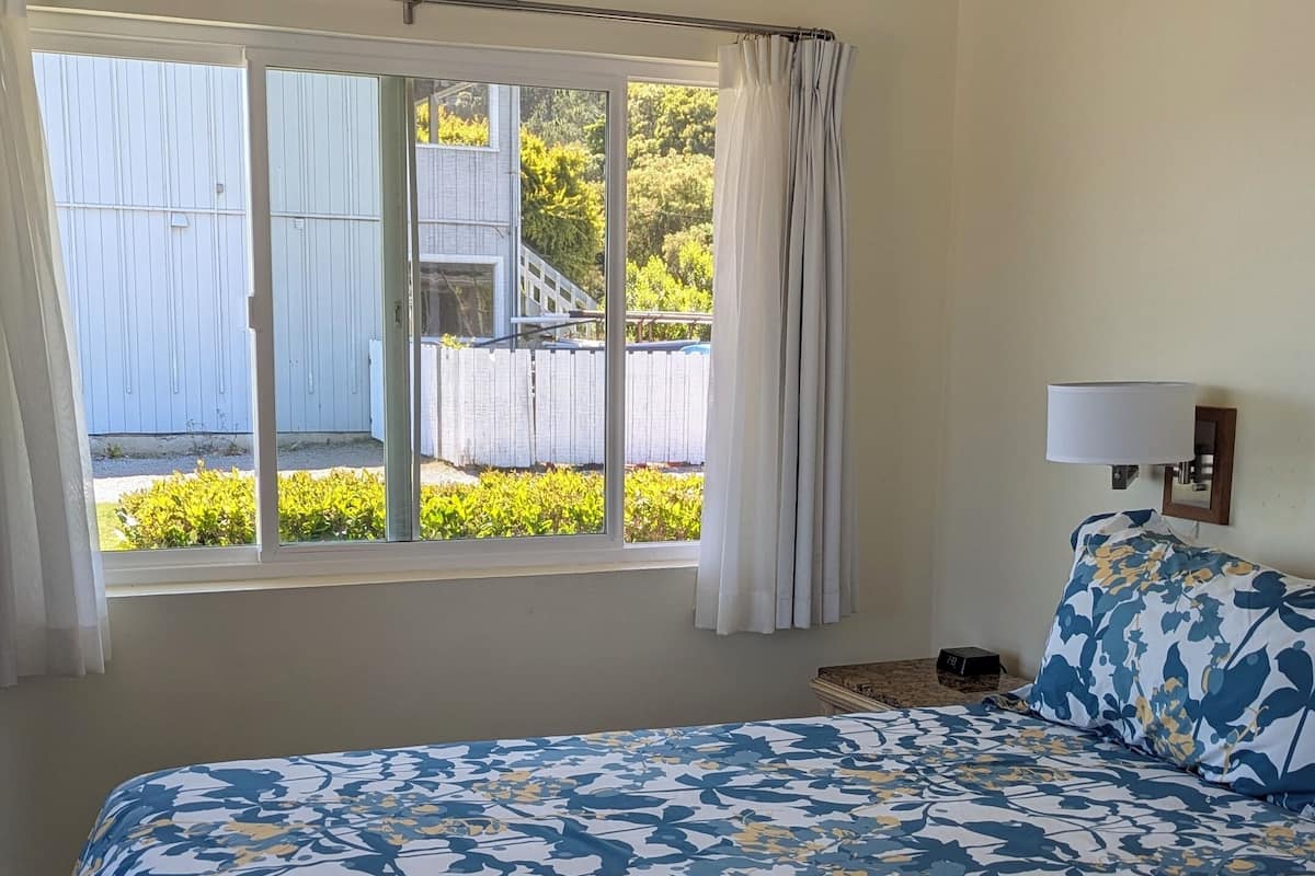 Une chambre avec un grand lit, une fenêtre avec des rideaux et une vue sur la verdure.