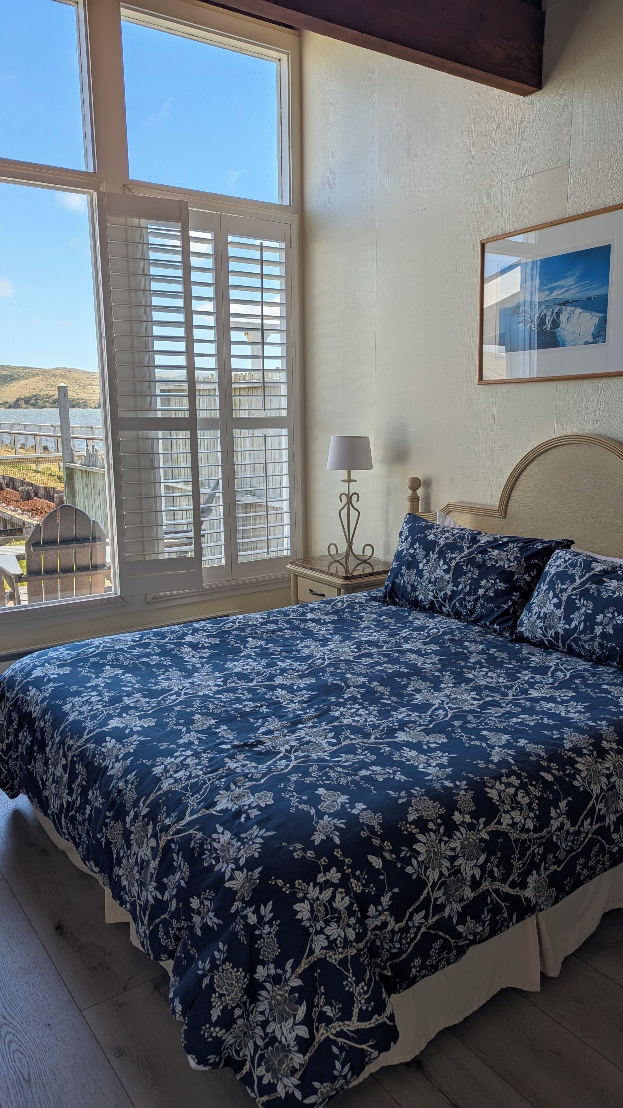 A bedroom with a large bed, a nightstand, a lamp, and a framed picture on the wall.