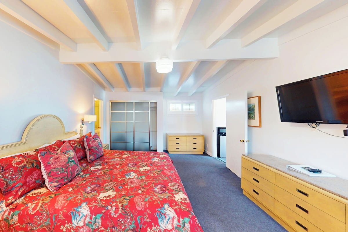 Une chambre à coucher comprenant un lit, une armoire, un téléviseur et une porte donnant sur une autre pièce.