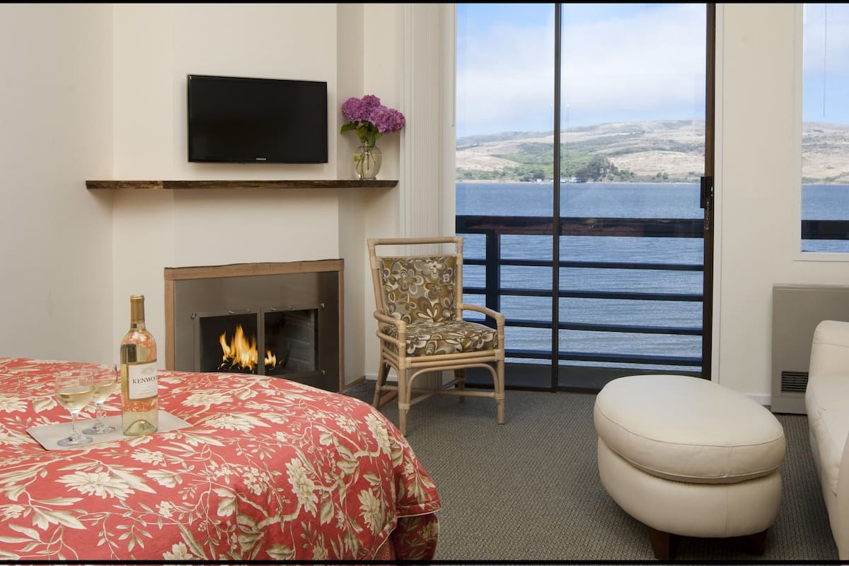 Une chambre d’hôtel avec un lit, une chaise, un canapé, une télévision, une cheminée et une vue sur la mer.