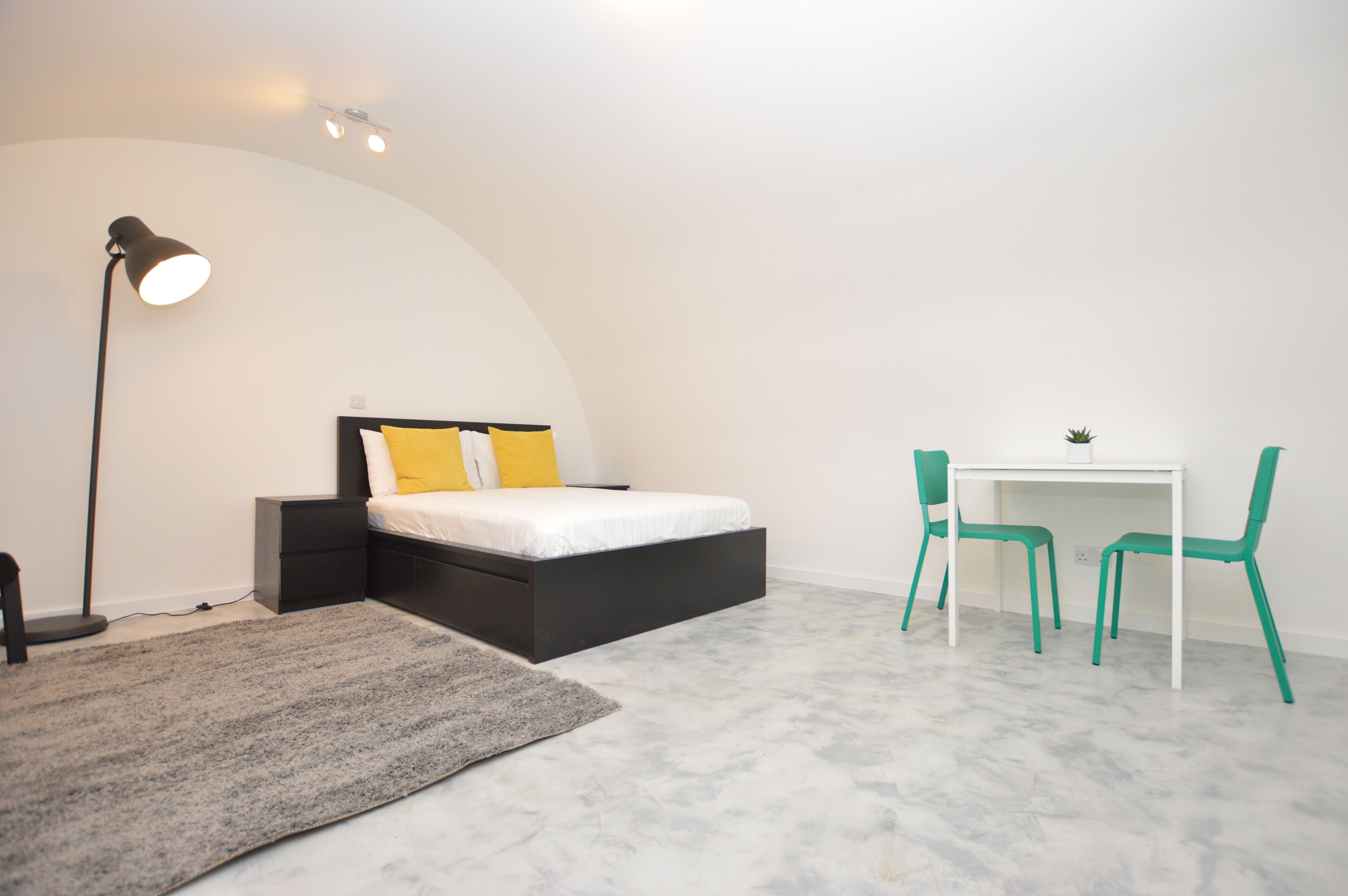 A bedroom with a bed, bedside table, lamp, desk, and two chairs.