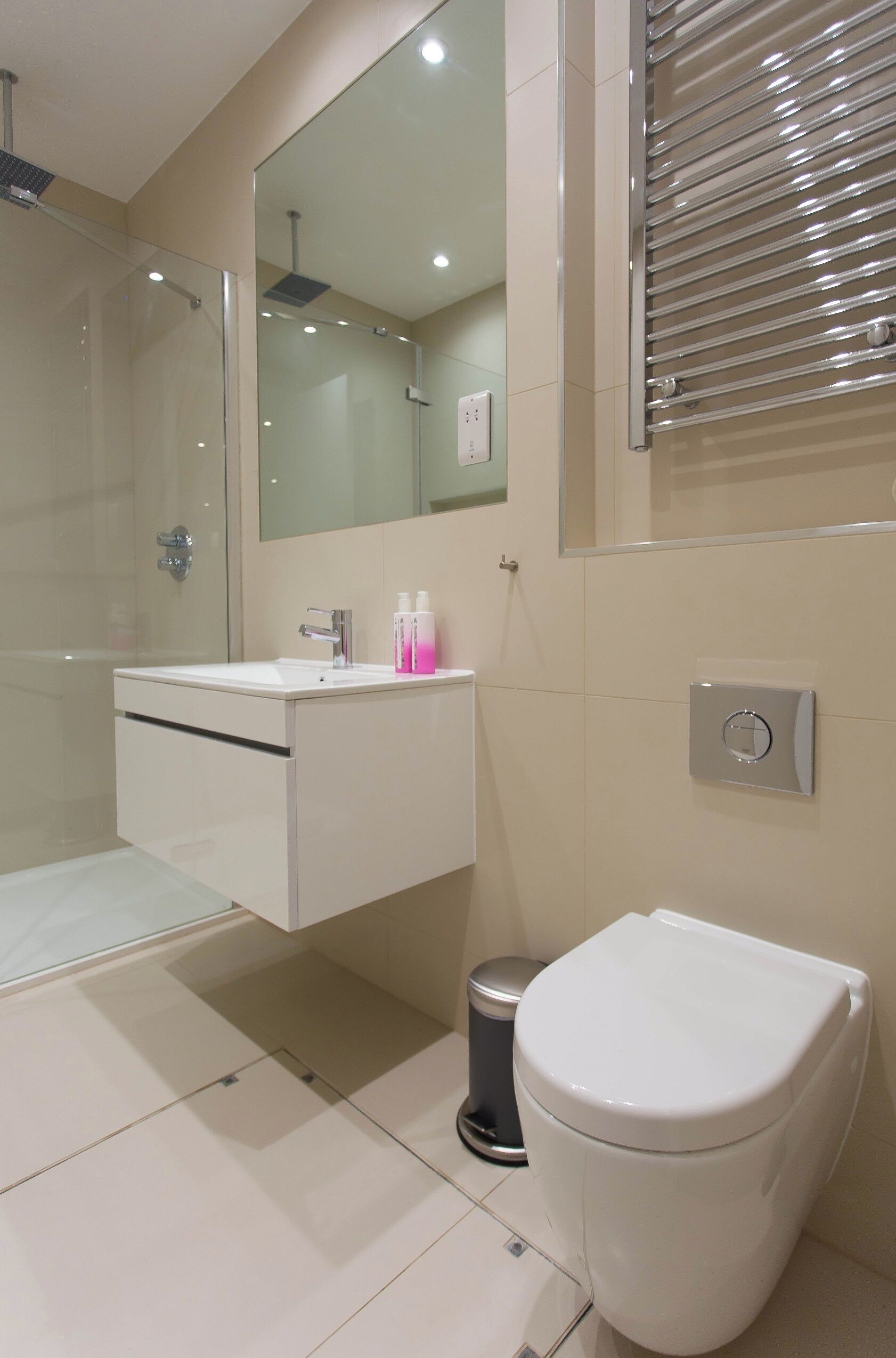 A modern bathroom with a glass shower enclosure, a white sink with a mirror above it, and a toilet with a flush button.