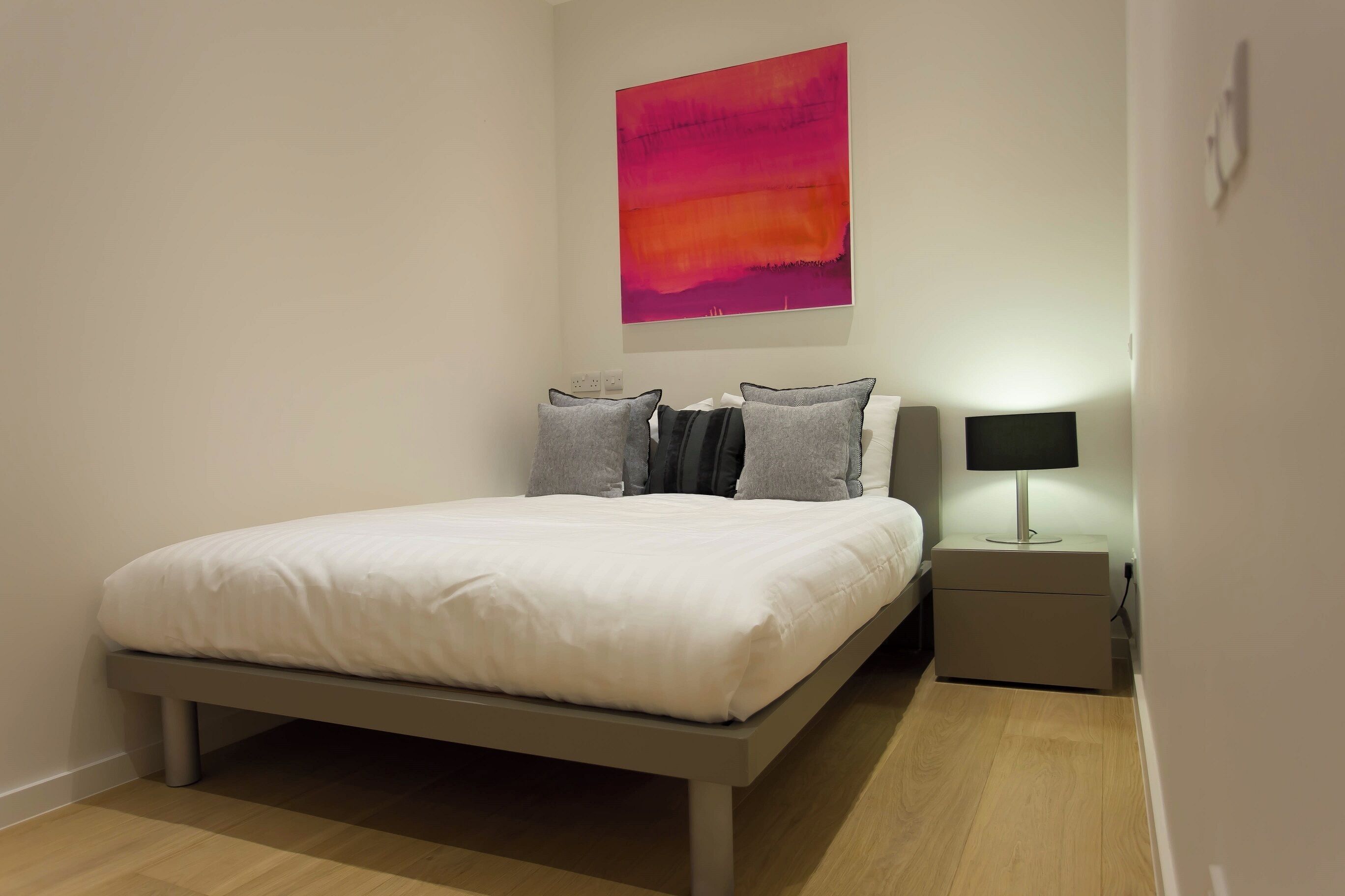 Une chambre à coucher moderne avec un lit, des tables de chevet et un tableau abstrait accroché au mur.