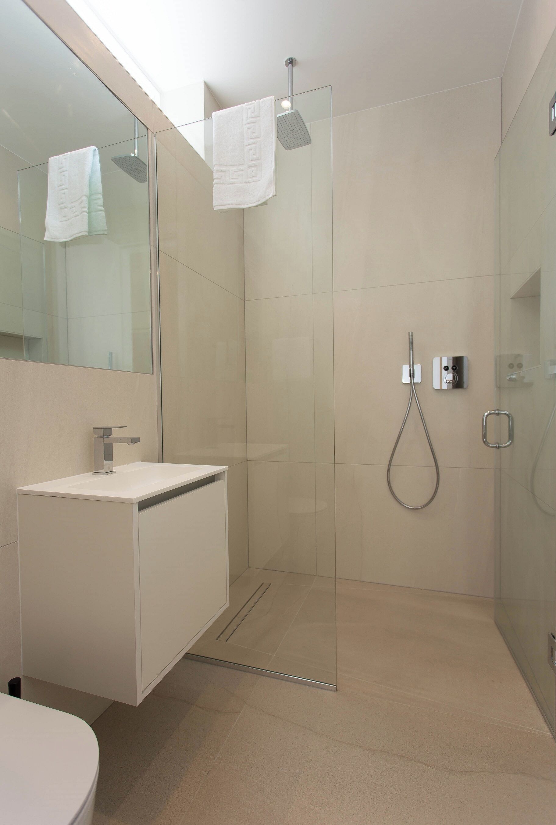 A modern bathroom with a glass-enclosed shower, a white sink, and a large mirror.