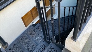 En svartmålad metalltrappa med intrikata mönster, som leder upp till en trädörr.