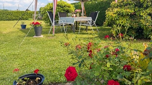 Un espace extérieur aménagé avec une tente, une table et des chaises, entouré de verdure et de plantes en pot.