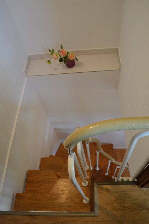 A wooden staircase with a handrail and a vase of flowers on the landing.