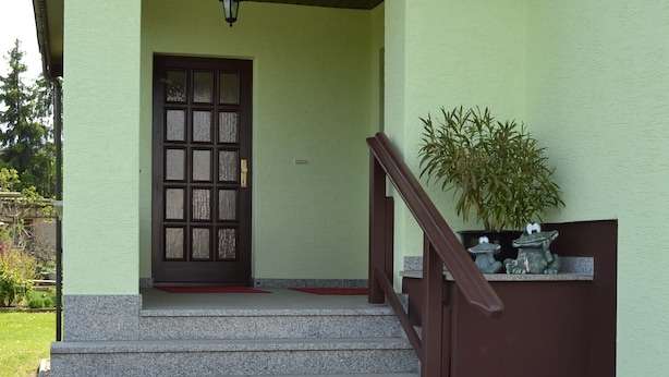 Un bâtiment à la façade verte, avec une porte marron et un escalier menant à un porche.