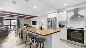 A modern kitchen with a central island, stainless steel appliances, and a large oven. - Luxury Condominium with Rustic Minimalist Style (Mont-Tremblant)