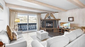 A cozy living room with a fireplace, a sofa, a television, and a balcony with a view of the mountains. - The `VIEW` a place for quality country living (Mont-Tremblant)
