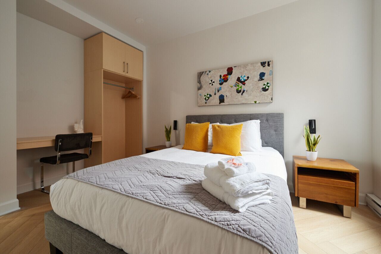 A modern bedroom with a bed, bedside tables, a desk, and a wardrobe.