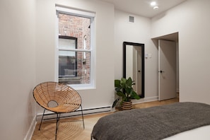 A room with a large window, a wicker chair, a potted plant, a mirror, and a door.
