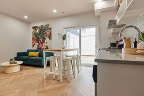 A modern kitchen with a dining area, a green sofa, and a large window.