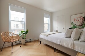 A bedroom with a bed, a chair, a potted plant, and large windows.
