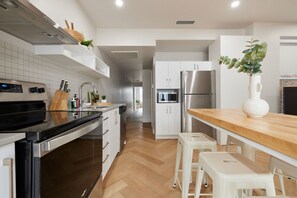 A modern kitchen with white cabinetry, stainless steel appliances, and a wooden countertop.