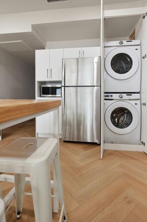 A compact kitchen with a stainless steel refrigerator, a microwave, and a double washing machine.
