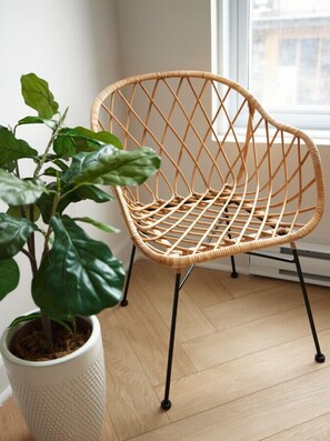 Une chaise en osier, dotée d’un dossier tressé et de pieds noirs, est placée à côté d’une plante en pot aux grandes feuilles.