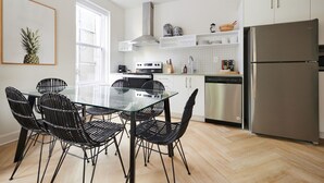 A modern kitchen with white cabinets, a stainless steel refrigerator, a glass dining table with black chairs, and a window providing natural light. - New and Cozy 3 bedroom in Le Plateau by Denstays (Montreal)