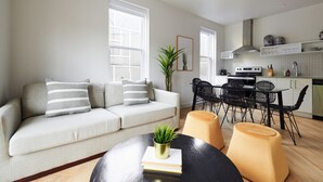 A modern living room with a sofa, a dining table, and chairs. There is a kitchen area with cabinets and a stove. - New and Cozy 3 bedroom in Le Plateau by Denstays (Montreal)