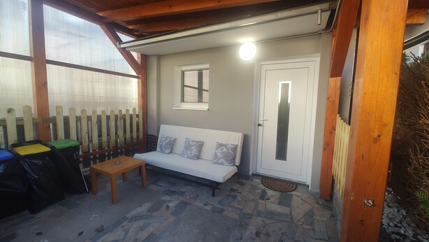 A covered outdoor seating area with a white sofa, a small table, and a trash bin. - Vu's Home - Apartment Junior - 40m2 (Hlavní město Praha)