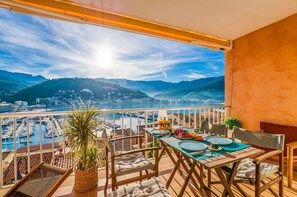 Een balkon met een tafel gedekt voor twee, met uitzicht op een jachthaven en stadsbeeld, met bergen op de achtergrond.