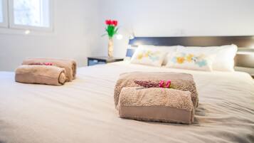 Een net opgemaakt bed met opgerolde handdoeken en een decoratieve bloemstelling op het nachtkastje.